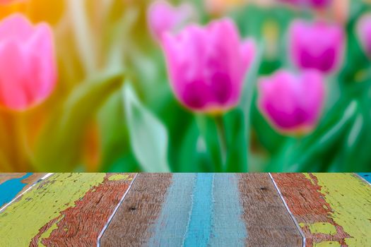 Empty vintage wooden table in font of blurry purple tulip in the garden and flare abstract background with copy space. Product display montage