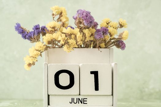 White cube calendar for june decorated with flowers over green background with copy space
