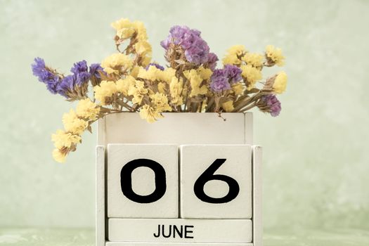 White cube calendar for june decorated with flowers over green background with copy space