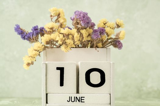 White cube calendar for june decorated with flowers over green background with copy space