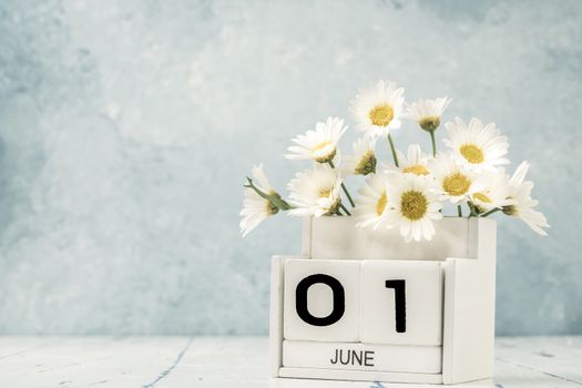 White cube calendar for june decorated with daisy flowers over blue background with copy space