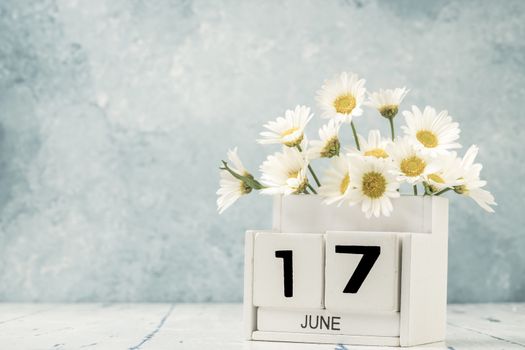 White cube calendar for june decorated with daisy flowers over blue background with copy space