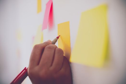 The hand is holding the post it notes attached to the wall. Concept brainstorming, share idea.