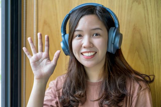 Asian Young woman waving hand for say hello when making video call to friend with social distancing, smiling female taking video blog recording vlog, Covid-19 pandemic, headphone and online meeting
