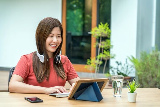 Asian business woman using technology tablet with keyboard and headphone for working from home in outdoor home and garden, startups and business owner, social distance and self responsibility