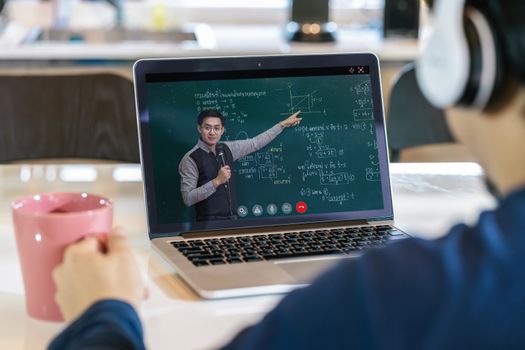 Rear View of Asian student learning with teacher over the physics formular in thai laguage on black board via video call conference when Covid-19 pandemic, education and Social distancing concept