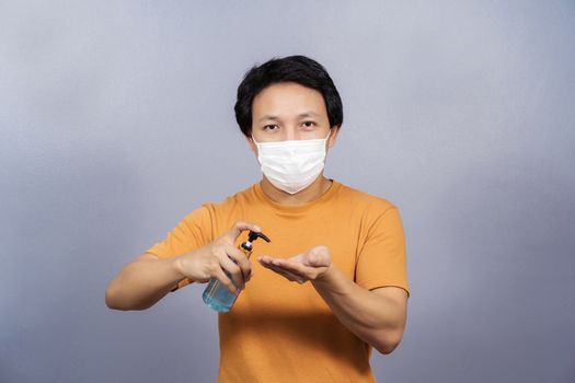 Asian man wearing face surgical mask presenting and using alcohol gel or hand sanitizer on blue color background, covid19 outbreak and pandemic,healthcare and protection against virus concept