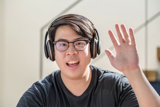 Asian business man waving hand for say hello when making video call to friend with social distancing, smiling female taking video blog recording vlog, Covid-19 pandemic, headphone and online meeting