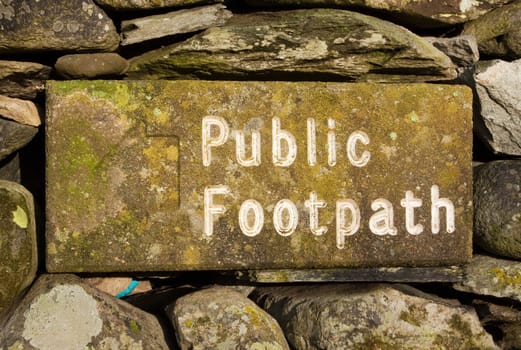 The stone public footpath sign is embedded in a dry stone wall and is situated alongside Ullswater lake in the English Lake District national park.