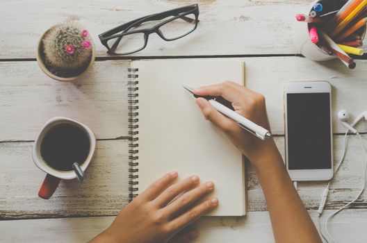 People are writing something in a white notebook with a cup of coffee and a telephone. On white wood floor