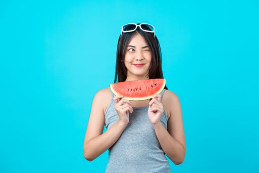 Attractive Asian young woman wearing summer vest and holding the Piece slide of watermelon on isolated blue color background, Sexy mouth bite, copy space and studio, fashion travel and tourist concept