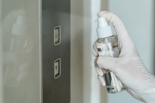 Closeup Asian woman hand wearing medical gloves and spraying Anti-Bacterial Sanitizer Spray to the elevator button before cleaning press, Coronavirus Network Outbreak, health care and cleaning covid19