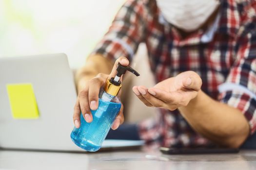 Closeup Asian man using hand sanitizer by pumping alcohol gel and washing before start to work with laptop in work from home period,coronavirus or covid19 outbreak,social distancing and responsibility