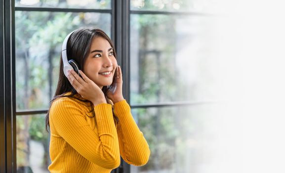 Happiness Asian smiling young woman wearing technology wireless headphones for listening the music via smart mobile phone in coffee shop or coworking space, Lifestyle and leisure with hobby concept