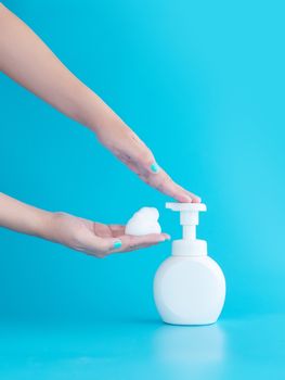plastic pump bottle and mousse foam or cleansing foam on woman hand isolated on blue background, vertical with copy space. cleaning concept