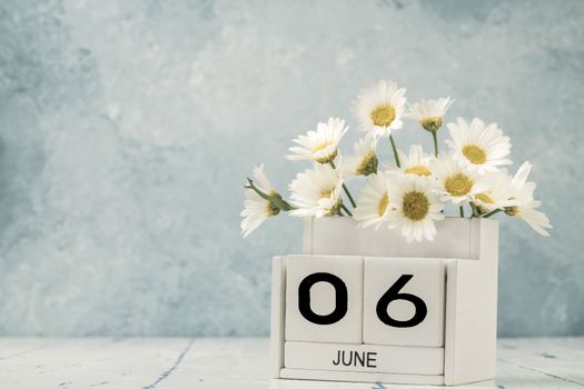 White cube calendar for june decorated with daisy flowers over blue background with copy space