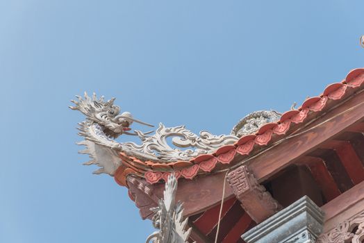 Typical cornice roof of Asian temple with dragon head shape, ancient tile roof and wooden structure. Look up view traditional pagoda exterior in the North Vietnam.