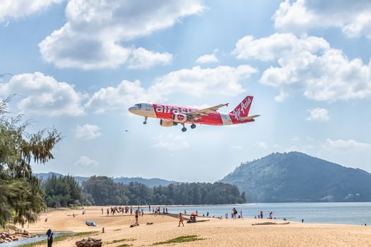 PHUKET, THAILAND - FEBRUARY 1, 2020: AirAsia aircraft ready for landing with many tourists visiting the plane landing spot and enjoy taking pictures of the plane at Mai Khao Beach, near Phuket Airport