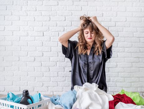 Laundry concept. Tired young woman doing the laundry at home sitting at the pile of clothes