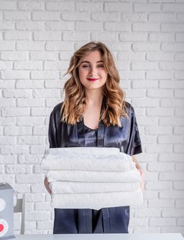 Laundry concept. Young beautiful woman in black pajamas holding a pile of clean white towels