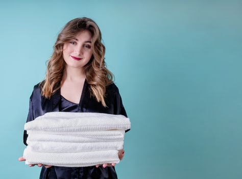 Laundry concept. Happy housewife holding a pile of clean white towels isolated on blue background with copy space