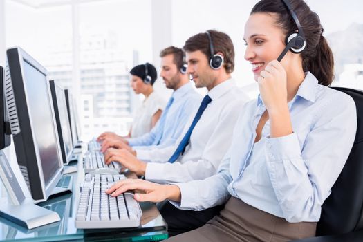 Side view of a group of business colleagues with headsets using computers at office desk