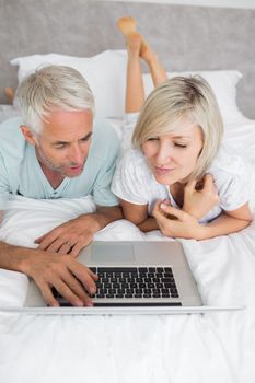 Relaxed mature couple using laptop in bed at home