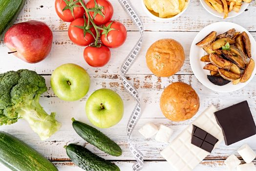 Healthy and unhealthy food concept. Fruit and vegetables vs sweets, burgers and potatoe fries top view flat lay on white rustic background