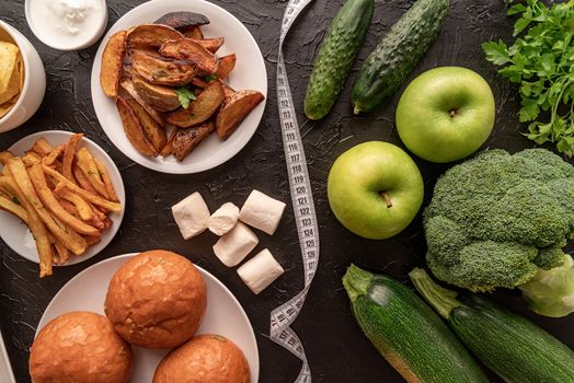 Healthy and unhealthy food concept. Fruit and vegetables vs sweets and potato fries top view flat lay with a measuring tape