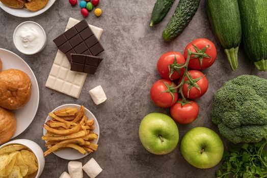 Healthy and unhealthy food concept. Fruit and vegetables vs sweets, burgers and potato fries top view flat lay on dark background