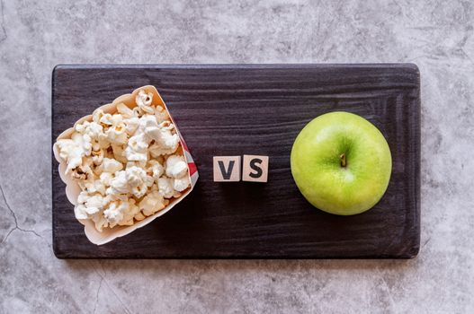 Healthy diet. Choosing between pop corn and apple top view on dark background