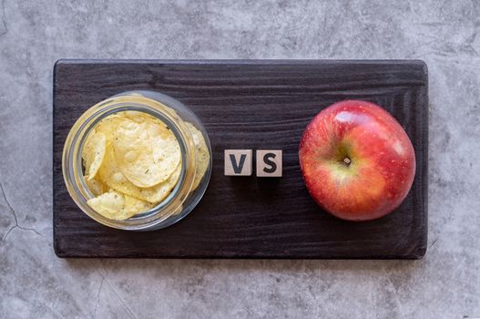 Healthy diet. Choosing between chips and apple top view on dark background