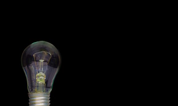 A light bulb on a black background to place text or illustration. The light bulb is a symbol of ideas, innovations, and new thoughts. 220 volt. Light bulb, business idea concept.