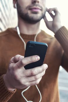 Smiling man listening to music on headphones and leaning against brick wall. Portrait of smiling man with headphones and cellphone standing by brick wall.