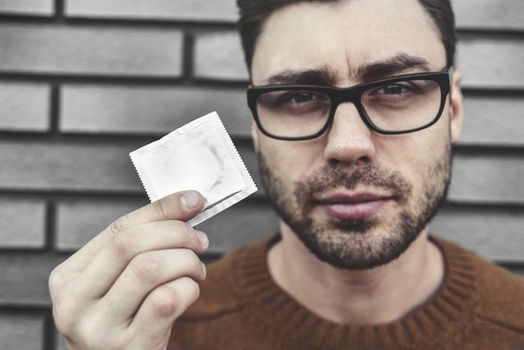 Contraception and healthy lifestyle concept. Male youngster with appealing look, holds condom. Bearded guy keeps contraceptive, advertises.