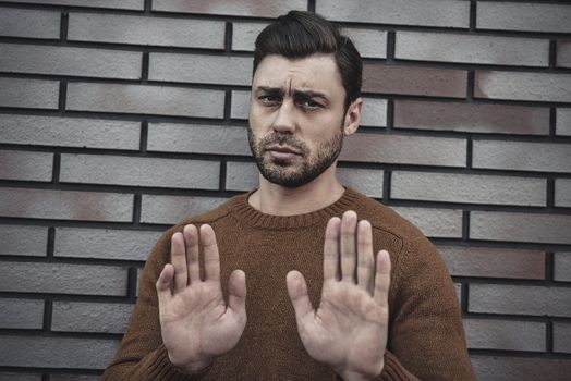 Young caucasian man standing on brick wall background afraid and terrified with fear expression stop gesture with hands, shouting in shock. Panic concept.