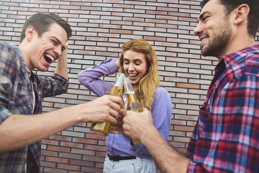 The three happy friends enjoying with beer on a brown brick wall background.