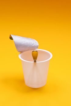 An empty clean yogurt cup with spoon on an orange background