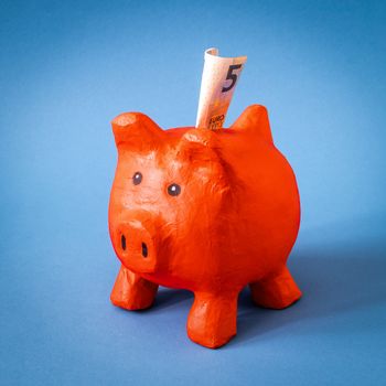 An image of a red papier mache piggy bank with 5 Euros