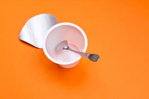 An empty clean yogurt cup with spoon on an orange background