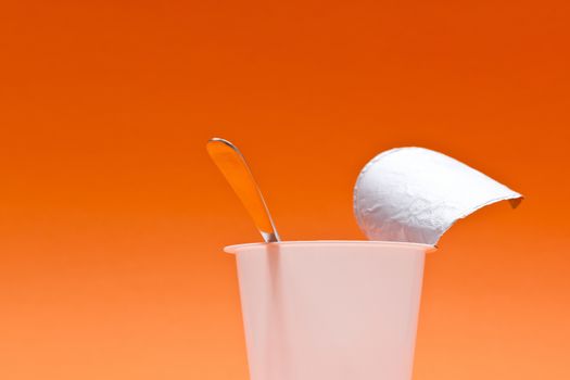 An empty clean yogurt cup with spoon on an orange background