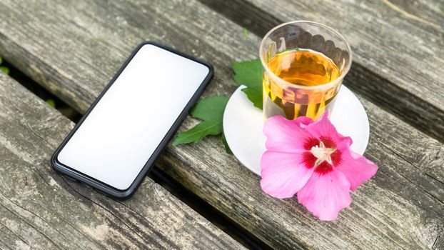 A mallow tea in a glass with smartphone on old wooden background