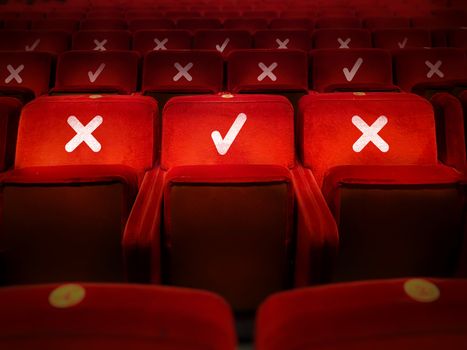 rows of empty chairs in a theater with the indication of where it is possible to sit to maintain the social safety distance during the period of the COVID-19 corona virus pandemic. Social distancing