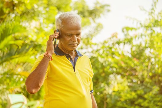 Elder man busy in mobile - Healthy senior Indian on phone outdoor at park, Morning - Happy male parent talking on phone