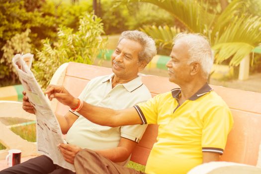 Two happy senior men reading newspaper at park outdoor - elderly friends enjoying moring news - Concept of happy older men lifestyle