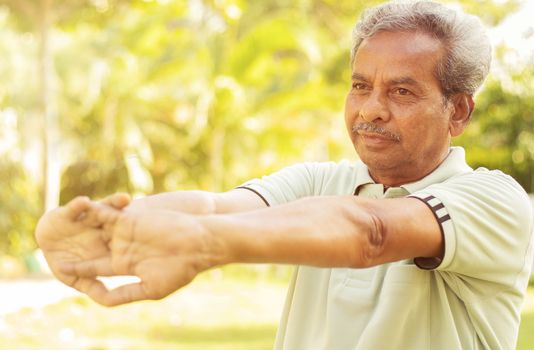 Senior man stretches hands before exercise - Concept of elderly person fitness outdoor - 60s person doing yoga asana at park