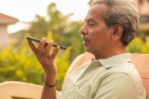 Senior man using virtual assistant in phone - Indian elder man using voice command on mobile - old man talking on smartphone at outdoor