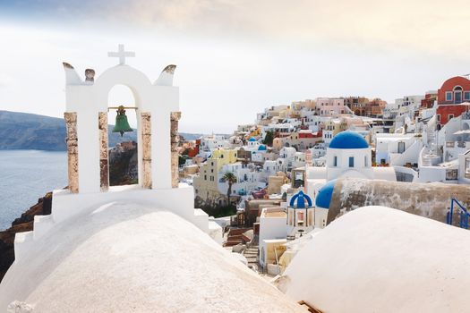 View of sea and Oia village  through traditional Greek white church arch with cross and bells in Oia village of Cyclades Island, Santorini
