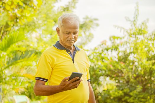 senior man looking the phone - old male person using mobile at park - elderly citizen on smartphone outdoor