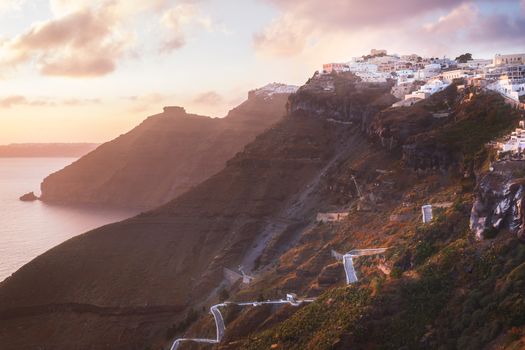 Sunset on the Greek Island of Santorini,with colorful  warm light and clouds over the town. The view follows the edge of the caldera from Thira, Skaros rock,  Imerovigli and Oia towards the sun